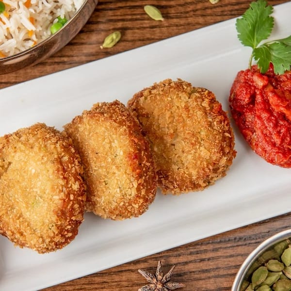 Three golden-brown Indian cutlets with red chutney and cilantro on a white plate.