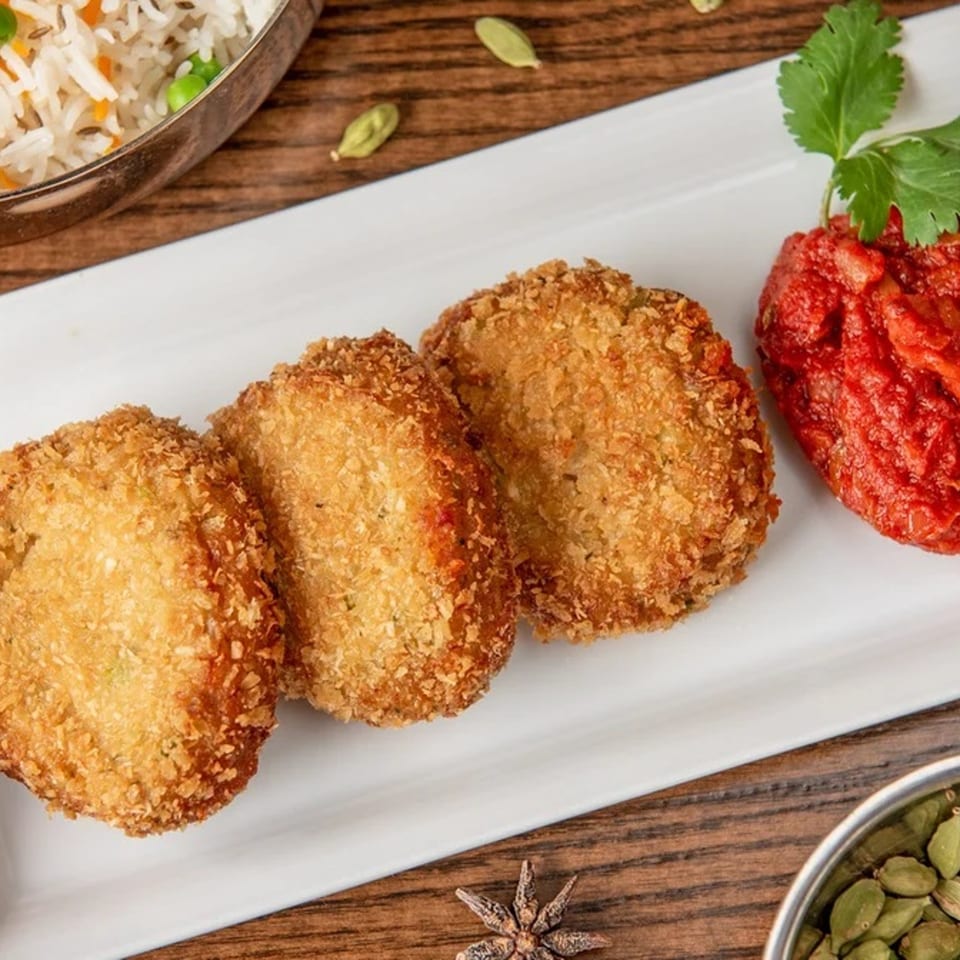 Three golden-brown Indian cutlets with red chutney and cilantro on a white plate.