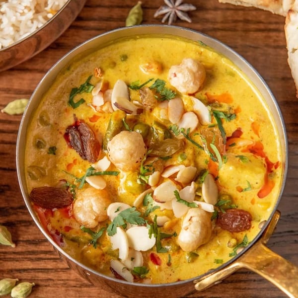 Coriander's Indian curry dish with nuts, raisins, and herbs, served in a metal bowl.