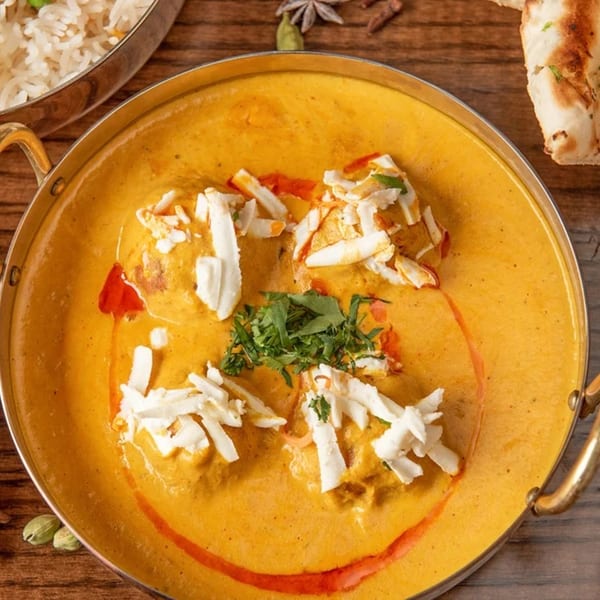 Indian Malai Kofta in a golden bowl, garnished with shredded paneer and fresh coriander.