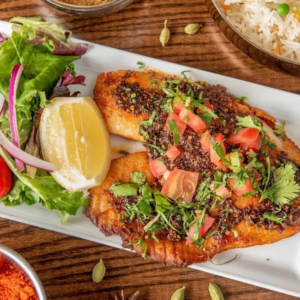 Coriander's Indian fish fry, garnished with tomatoes, cilantro, and a lemon wedge, served with salad.