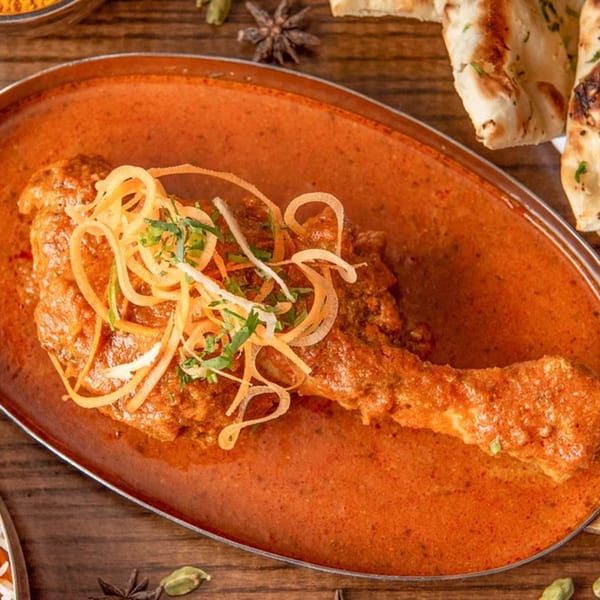 Indian chicken curry with a drumstick in a rich orange sauce, garnished with onions and herbs.
